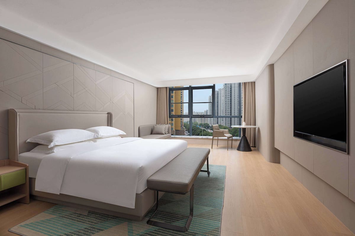 A modern hotel room with a large bed, a desk, a chair, and a TV.