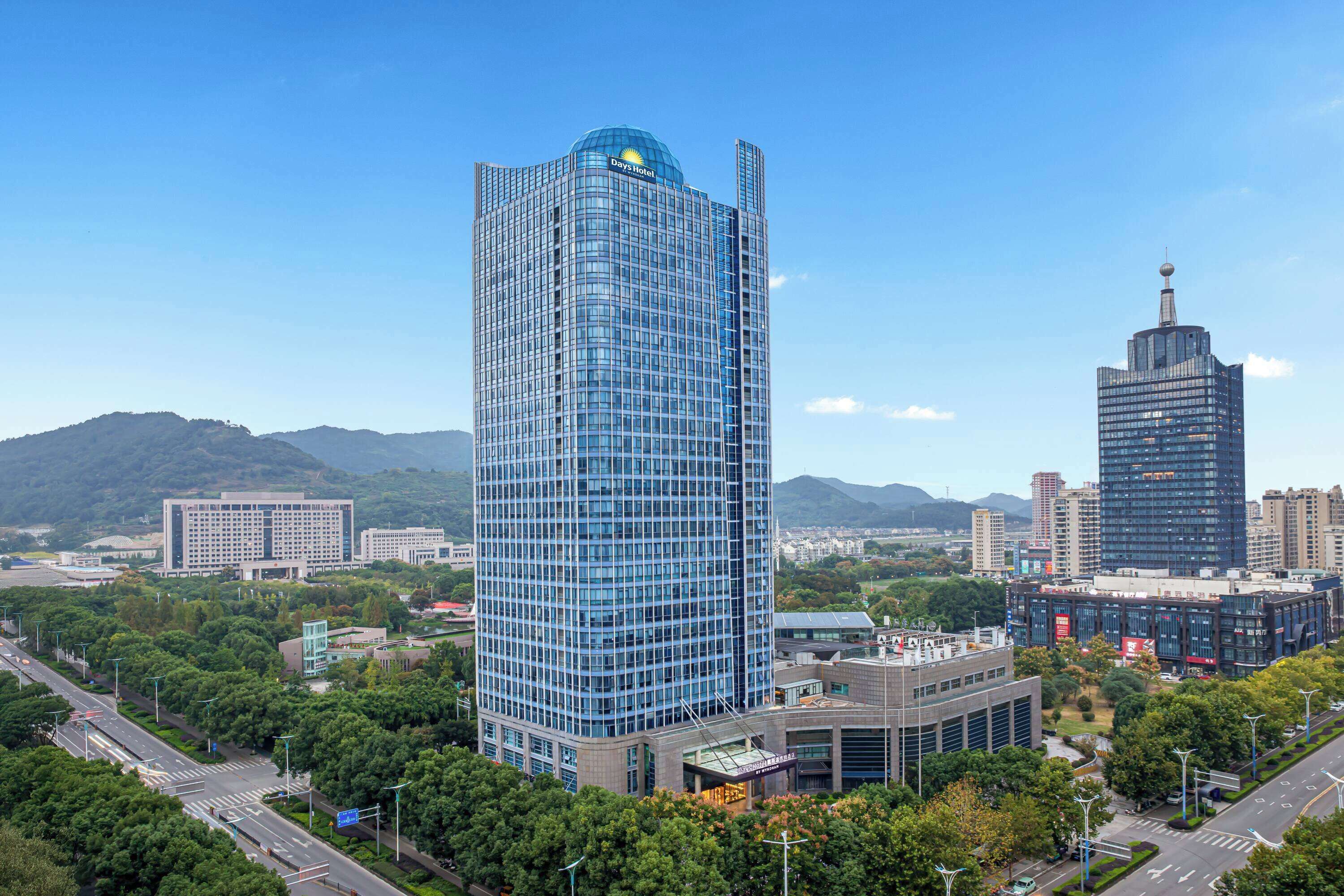A high-rise hotel with a modern glass facade, surrounded by lush greenery and other buildings.