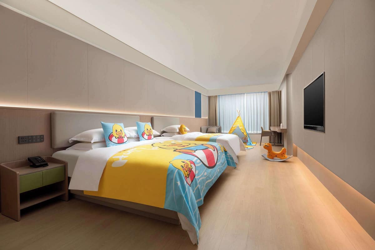 A modern hotel room with a large bed, bedside tables, a flat-screen TV, and a window with curtains.