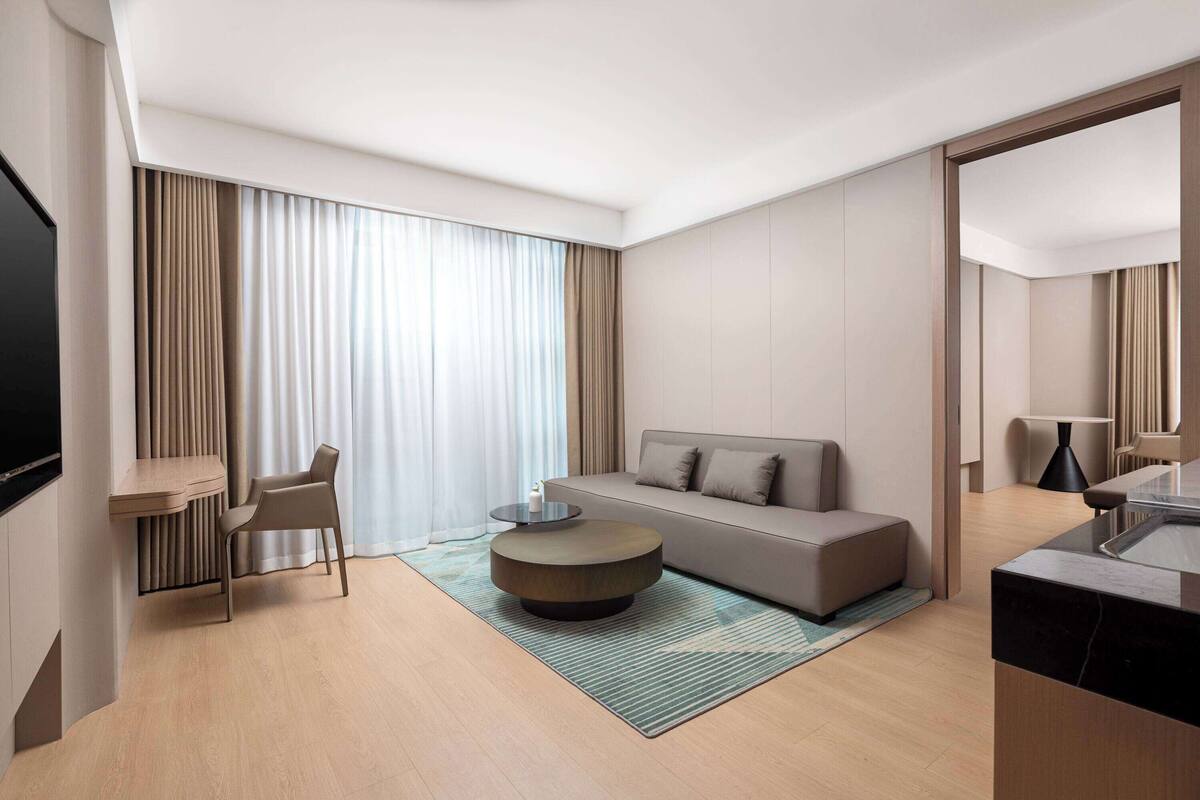 A modern hotel room with a sofa, a round coffee table, a chair, and a TV.