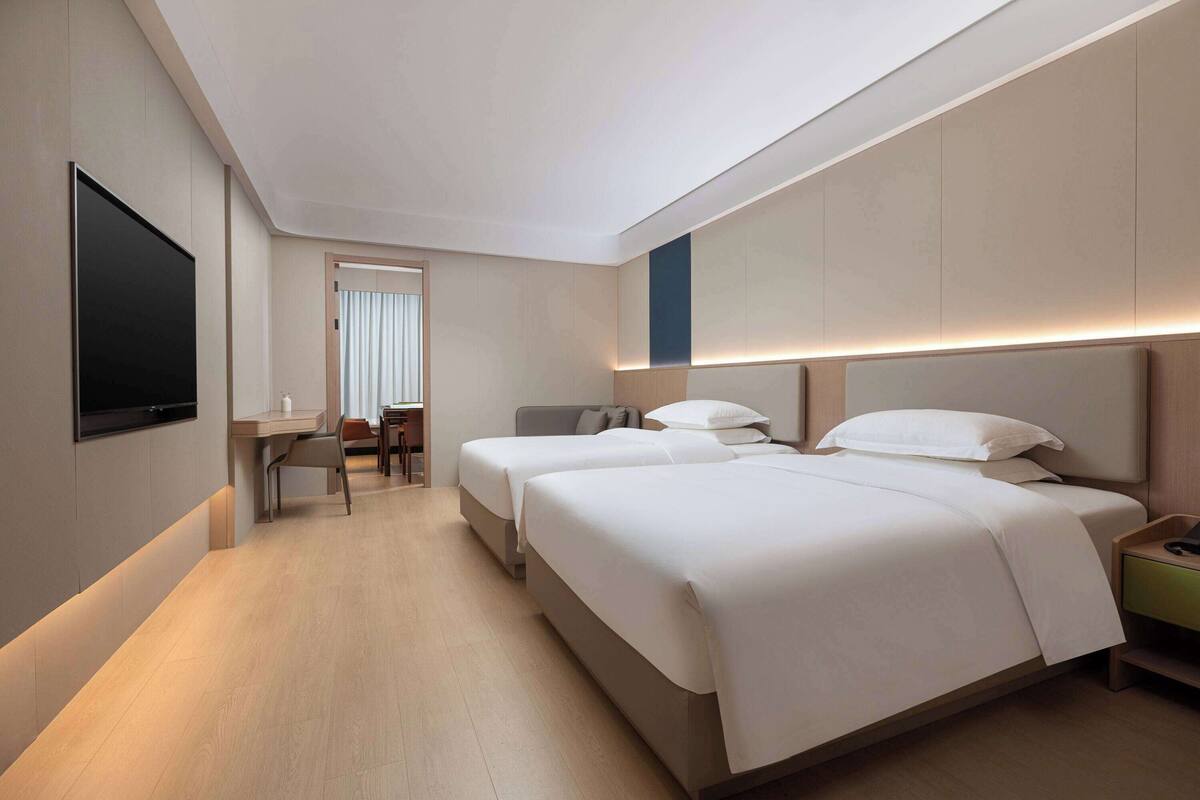 A modern hotel room with two beds, a flat-screen TV, a desk, and a chair.