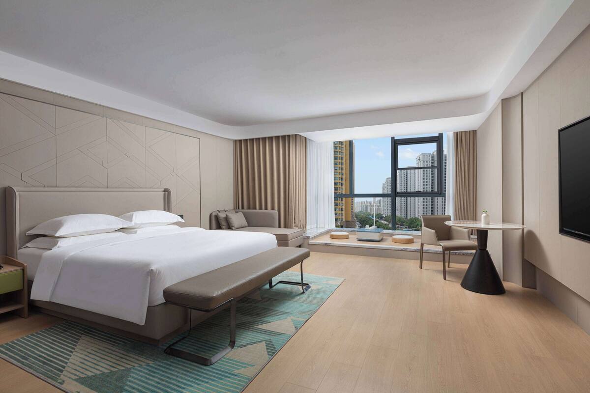 A modern hotel room with a large bed, a desk, a chair, and a TV.