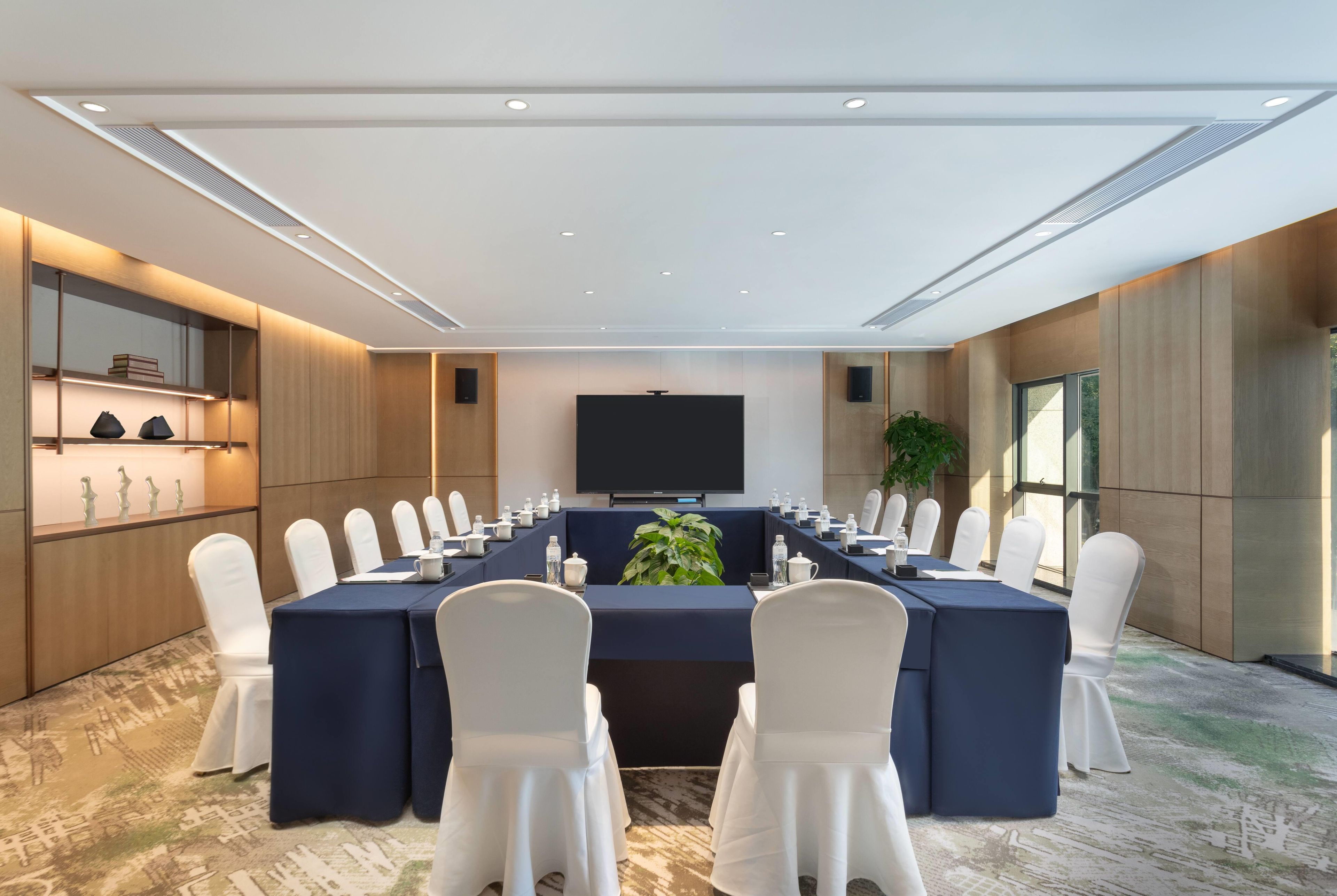 A conference room with a long table, white chairs, and a large screen.