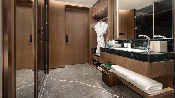 Un baño moderno con armarios de madera, cabina de ducha de vidrio, suelo de mármol, un espejo grande y un perchero.