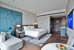 Habitación de hotel con una cama, un escritorio, una silla, un televisor y una mesita con fruta.
