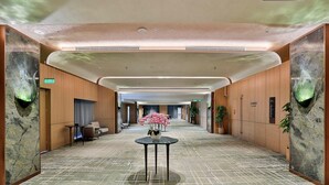 A hotel corridor with a patterned carpet, a round table with a vase, and wooden paneling on the walls. - Wyndham Garden Hangzhou Xixi (Hangzhou)