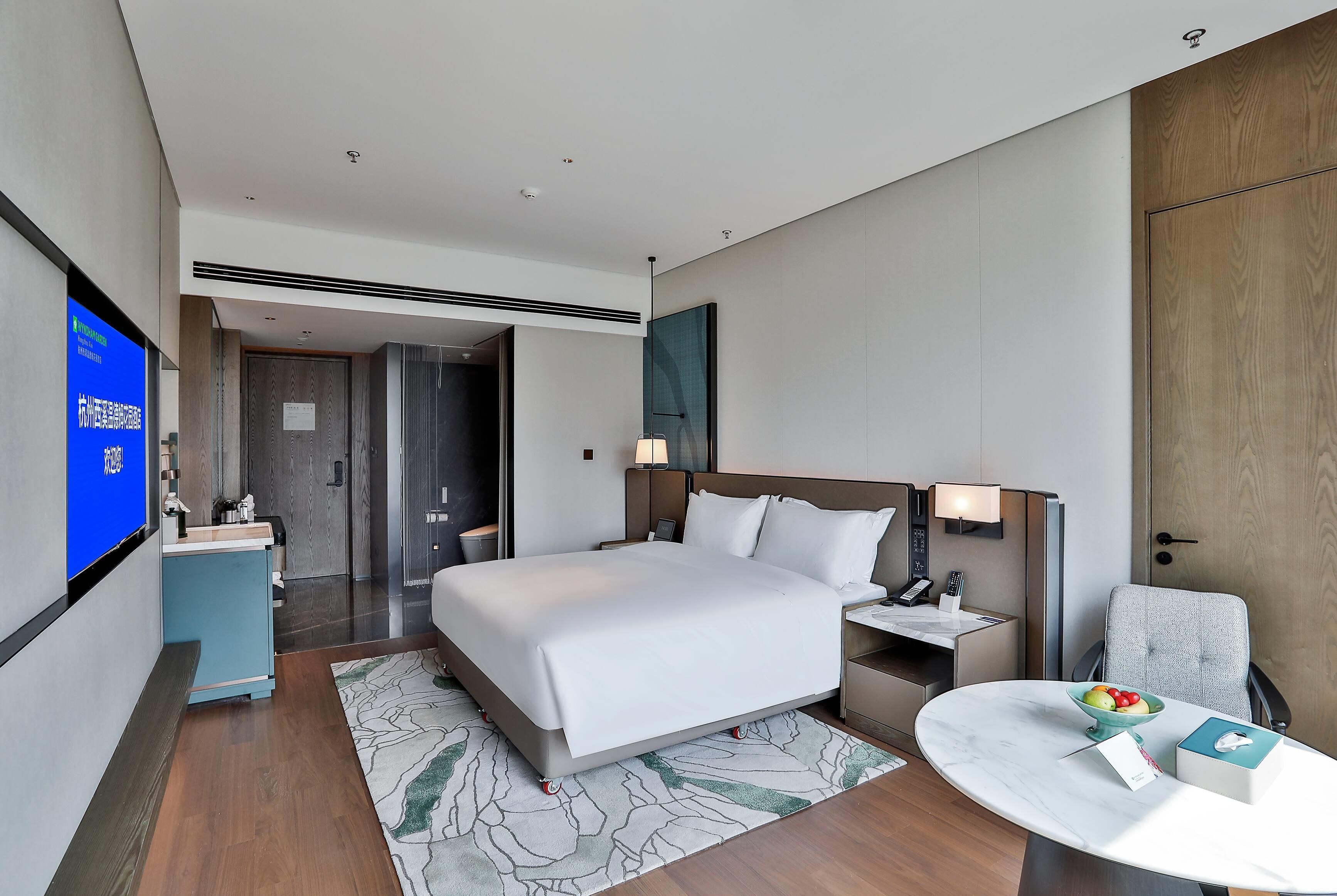 A hotel room with a bed, bedside tables, a desk, a chair, a TV, and a bathroom.