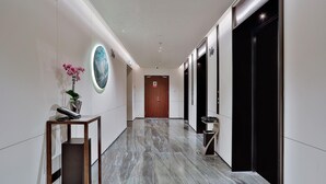 A modern hallway with a marble floor, a wooden door at the end, and a small table with a vase of flowers. - Wyndham Garden Hangzhou Xixi (Hangzhou)