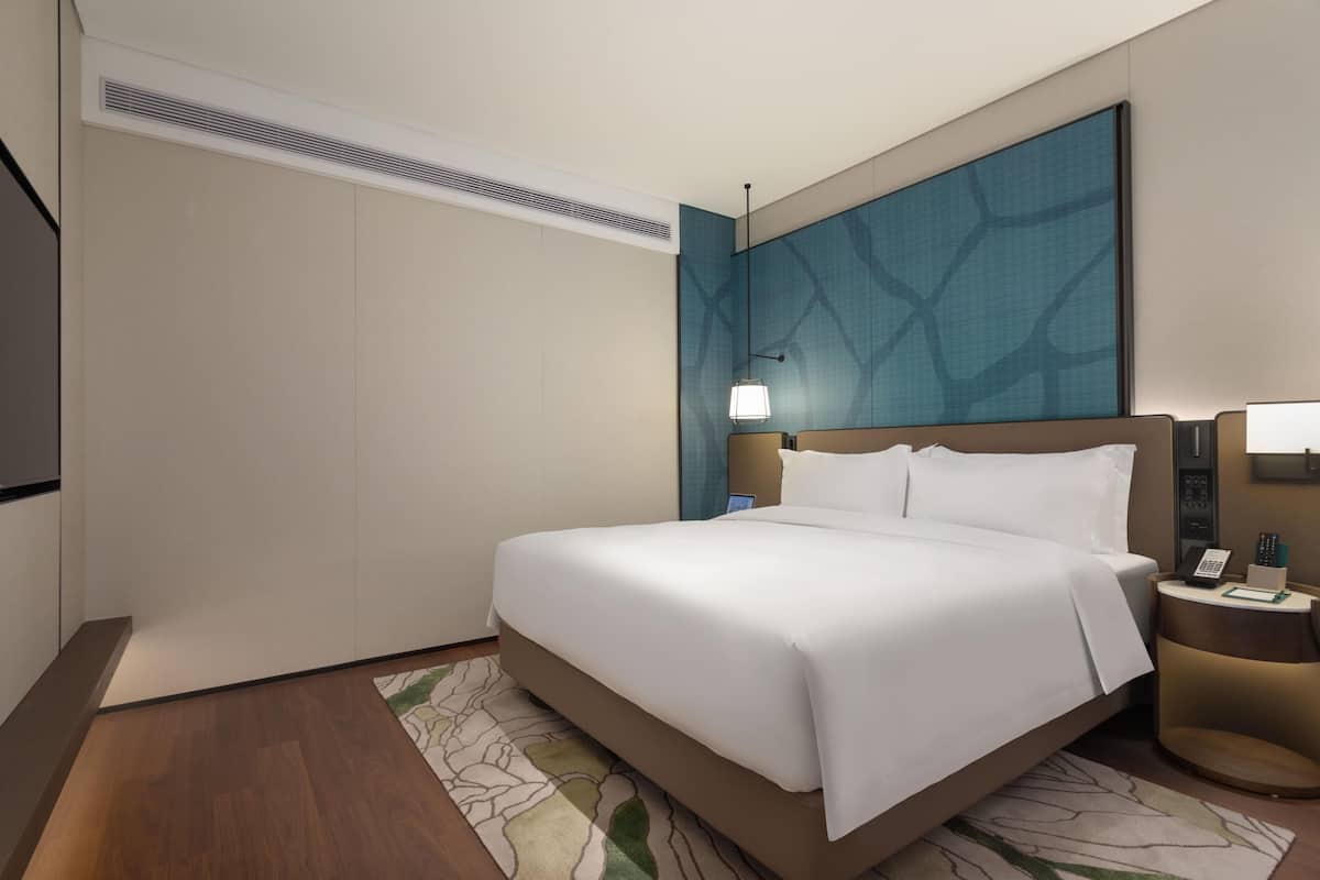 A hotel room with a bed, a nightstand, a lamp, and a wall-mounted TV.
