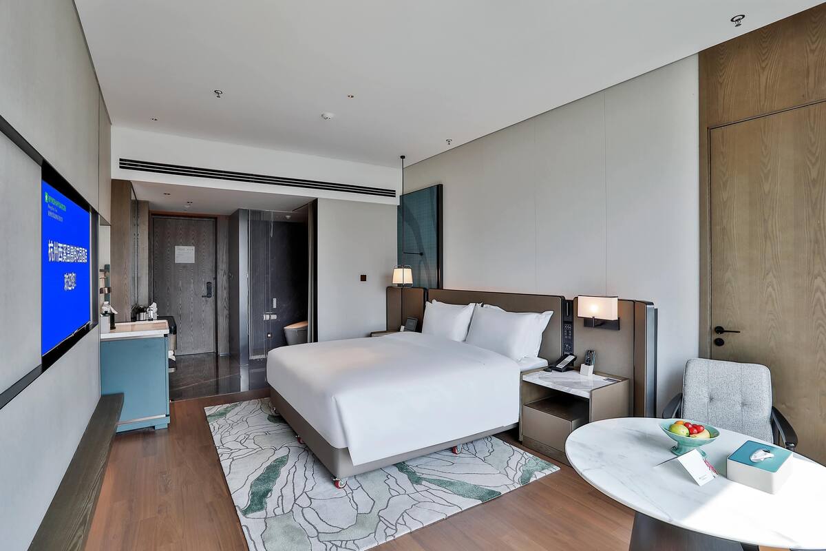 A modern hotel room with a large bed, bedside tables, a desk, and a TV.