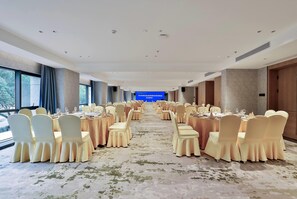 Un salón de banquetes con mesas redondas, sillas y una pantalla azul al frente.