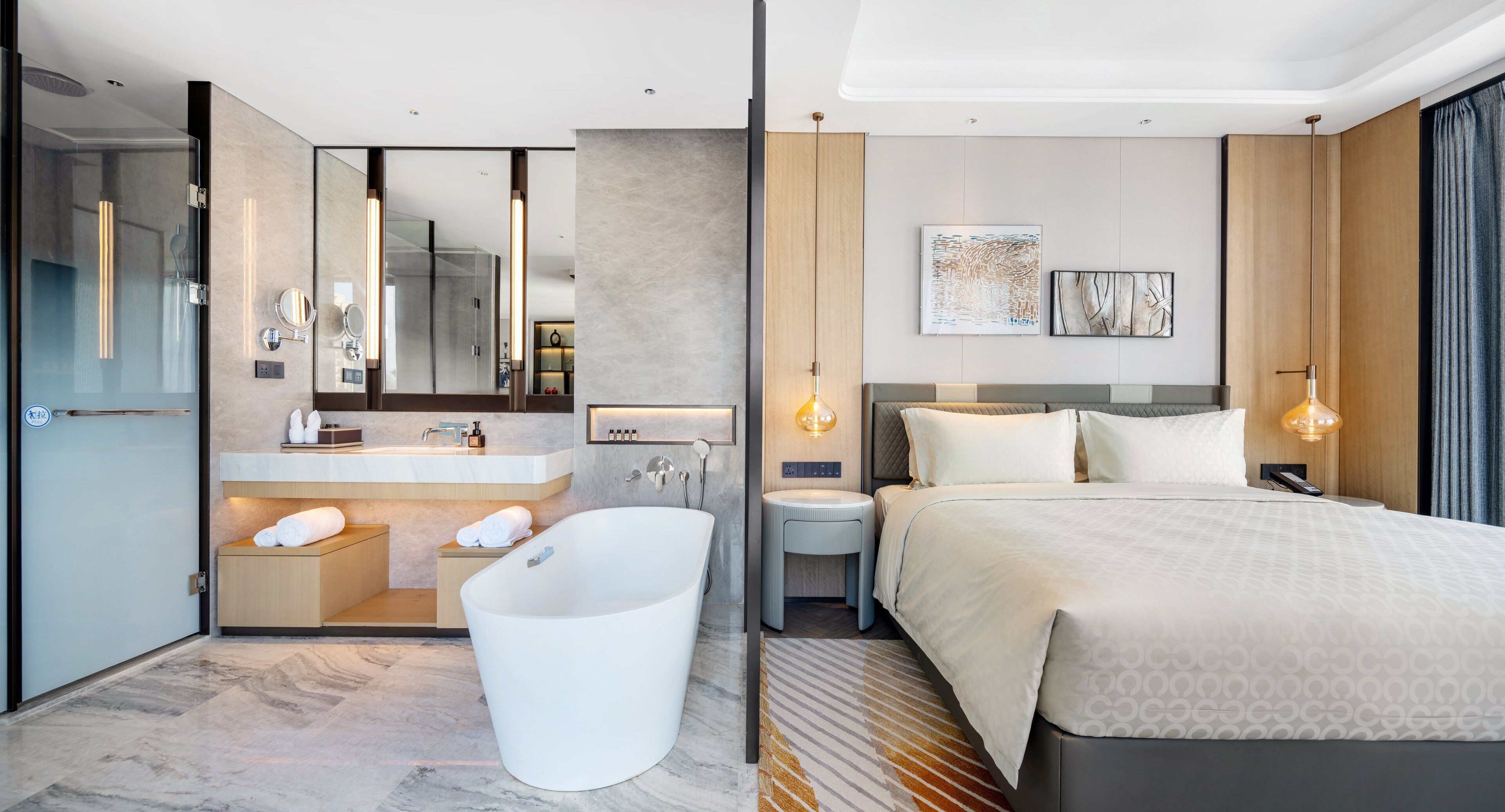 Una habitación de hotel moderna con una cama grande, baño independiente, tocador con espejo y un ventanal amplio.