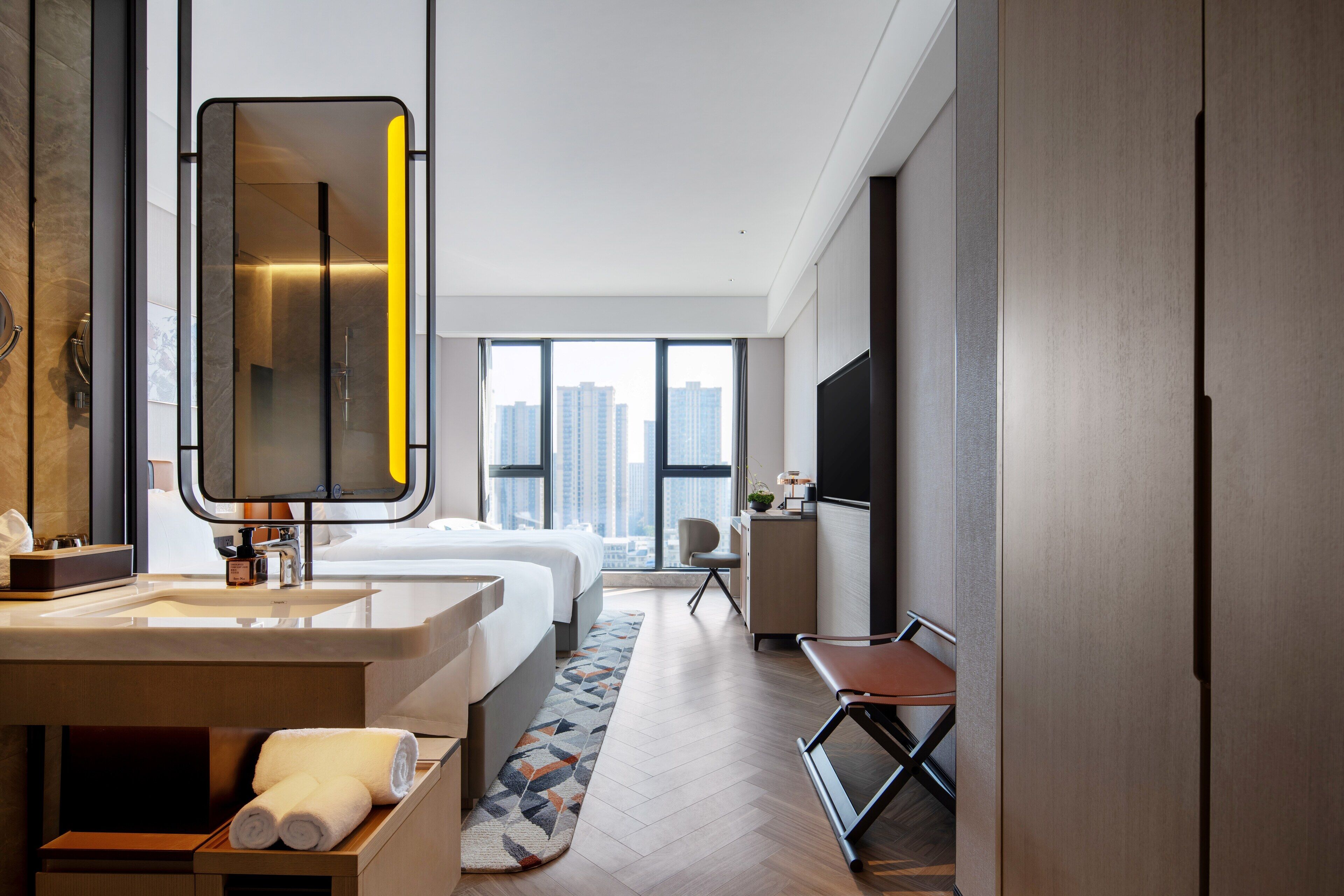 A modern hotel room with a large bed, a bathroom with a mirror and sink, a desk, and a TV.