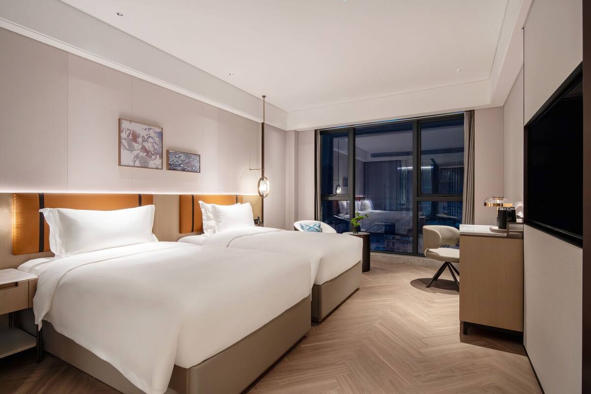 Habitación de hotel moderna con una cama grande, un escritorio y vistas a la ciudad a través de amplias ventanas.