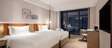 Habitación de hotel moderna con una cama grande, un escritorio y vistas a la ciudad a través de amplias ventanas.