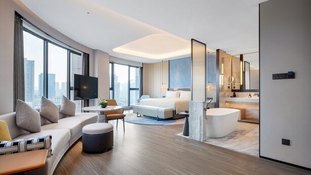 Une chambre d’hôtel moderne équipée d’un grand lit, d’un canapé, d’un bureau, d’une télévision et d’une salle de bain.