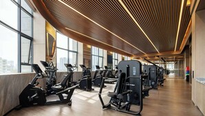 Une salle de sport moderne équipée de machines de cardio et de postes de musculation, dotée de grandes fenêtres et d’un plafond en bois.