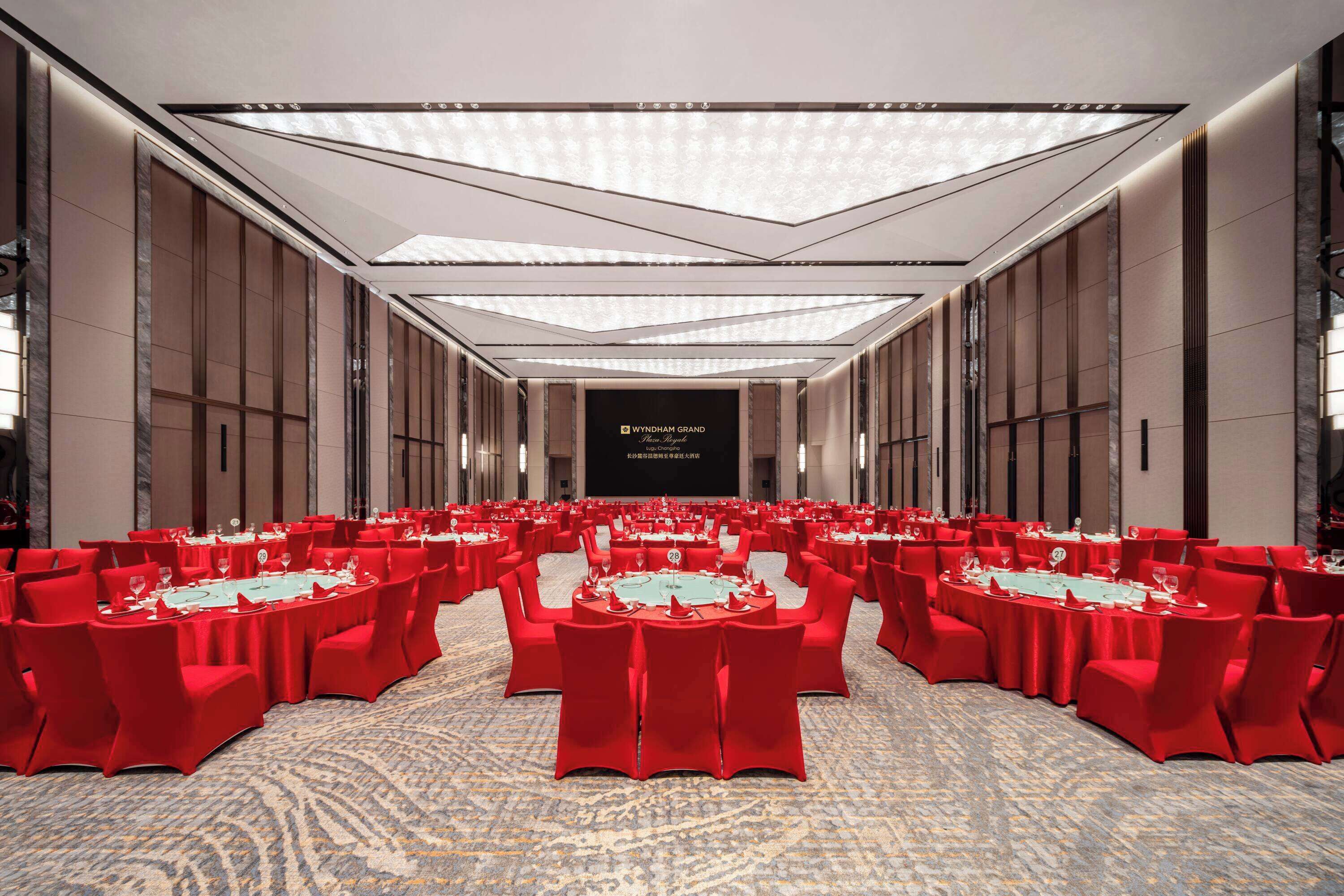 A large conference room with red chairs and tables, a high ceiling with recessed lighting, and a sign reading "WYNDHAM GRAND."