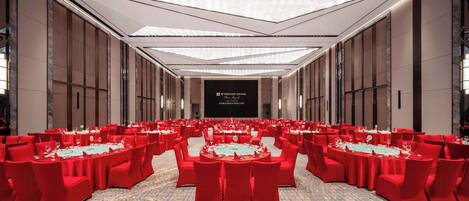 A large conference room with red chairs and tables, a high ceiling with recessed lighting, and a sign reading "WYNDHAM GRAND."