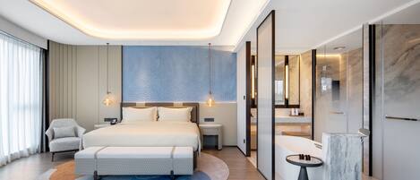 Una habitación de hotel moderna con una cama grande, una mesita de noche, una silla, una mesa redonda y un detalle decorativo de mármol.