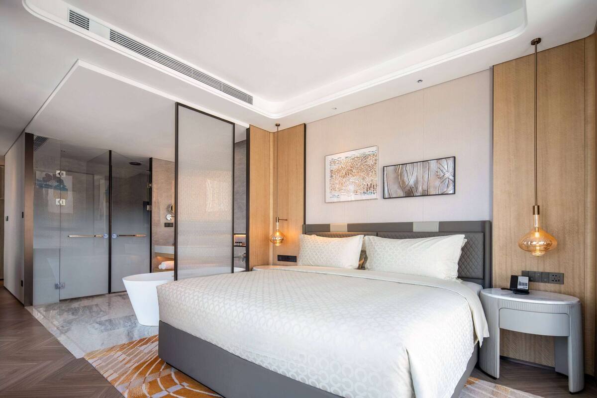 Una habitación de hotel moderna con una cama grande, una mesita de noche, una lámpara de pared y un espejo amplio.
