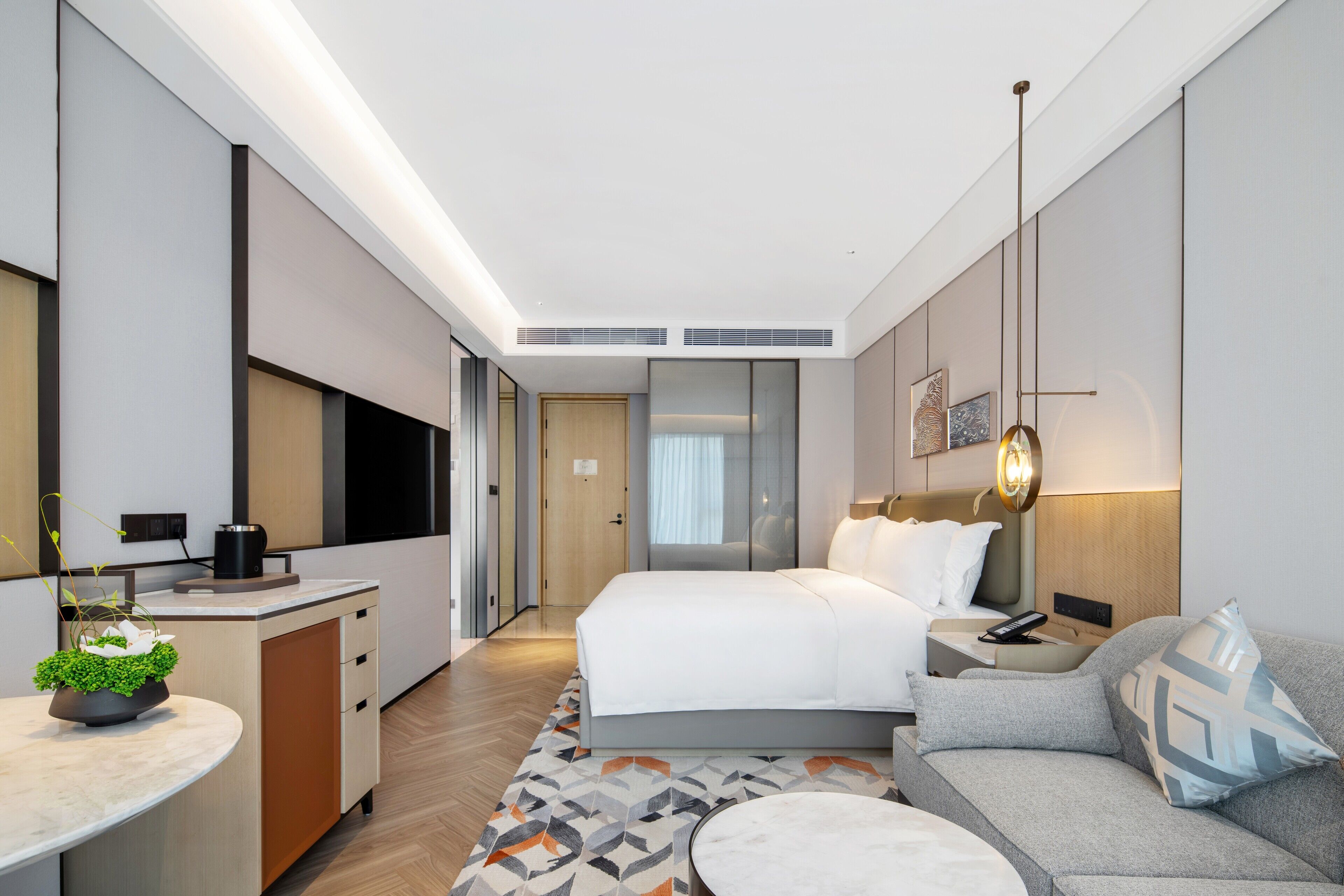 Ein modernes Hotelzimmer mit einem großen Bett, einer Couch, einem Schreibtisch mit Pflanze und einem Fernseher.