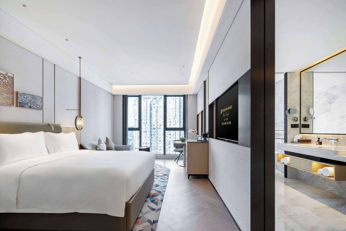 Una habitación de hotel moderna con una cama grande, un escritorio, un televisor y un baño con espejo y lavabo.