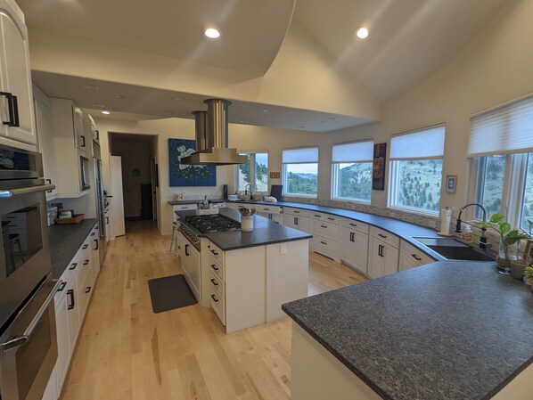 A modern kitchen with a curved island, stainless steel appliances, and large windows offering a view of the outdoors.