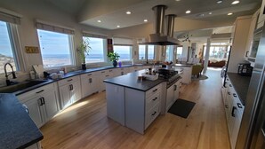 Een ruime keuken met een groot eiland, houten vloeren en uitzicht op de oceaan.