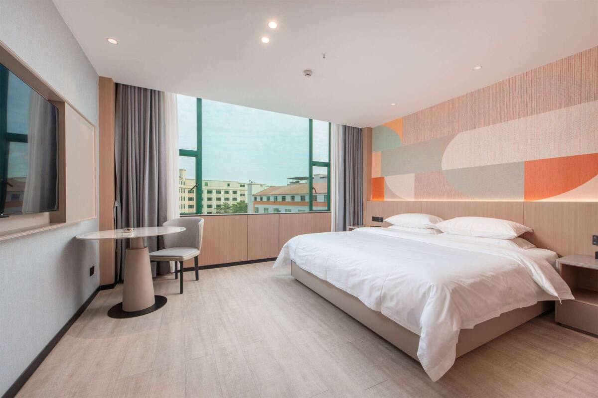 A modern hotel room with a large bed, a round table, and a view of the city.