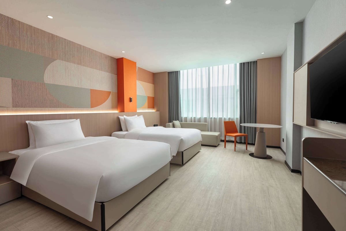A modern hotel room with two beds, a TV, a desk, and a large window with curtains.