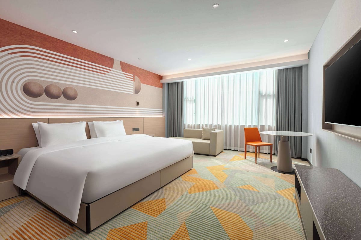 A modern hotel room with a large bed, a sofa, a TV, and a desk.