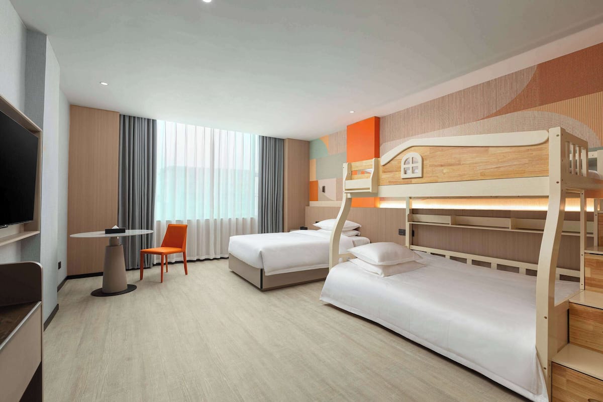 A hotel room with two bunk beds, a desk, an orange chair, and a TV.