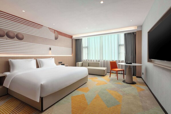 Una habitación de hotel moderna con una cama grande, un sofá, un televisor y una mesa de comedor.