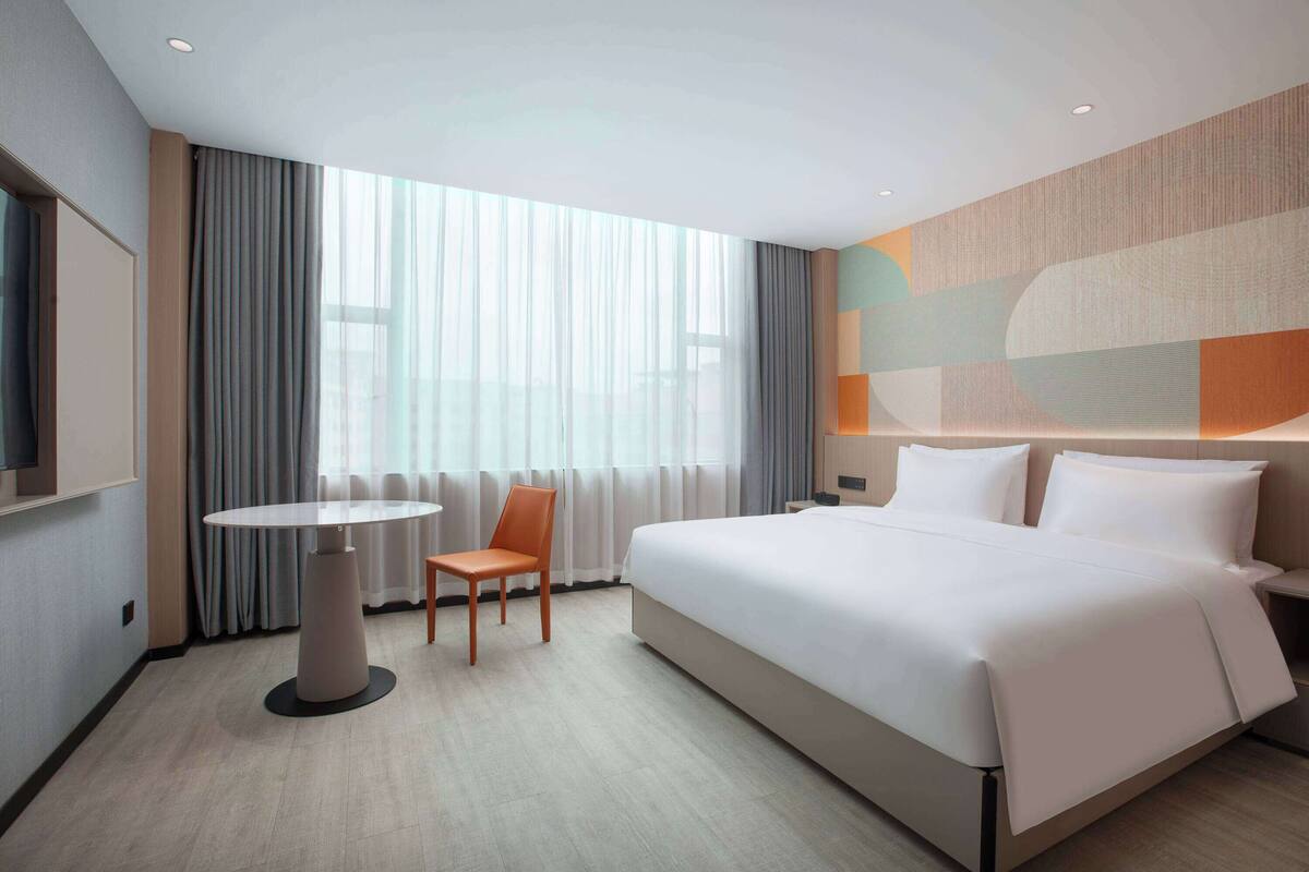 A modern hotel room with a large bed, a round table, and a chair.