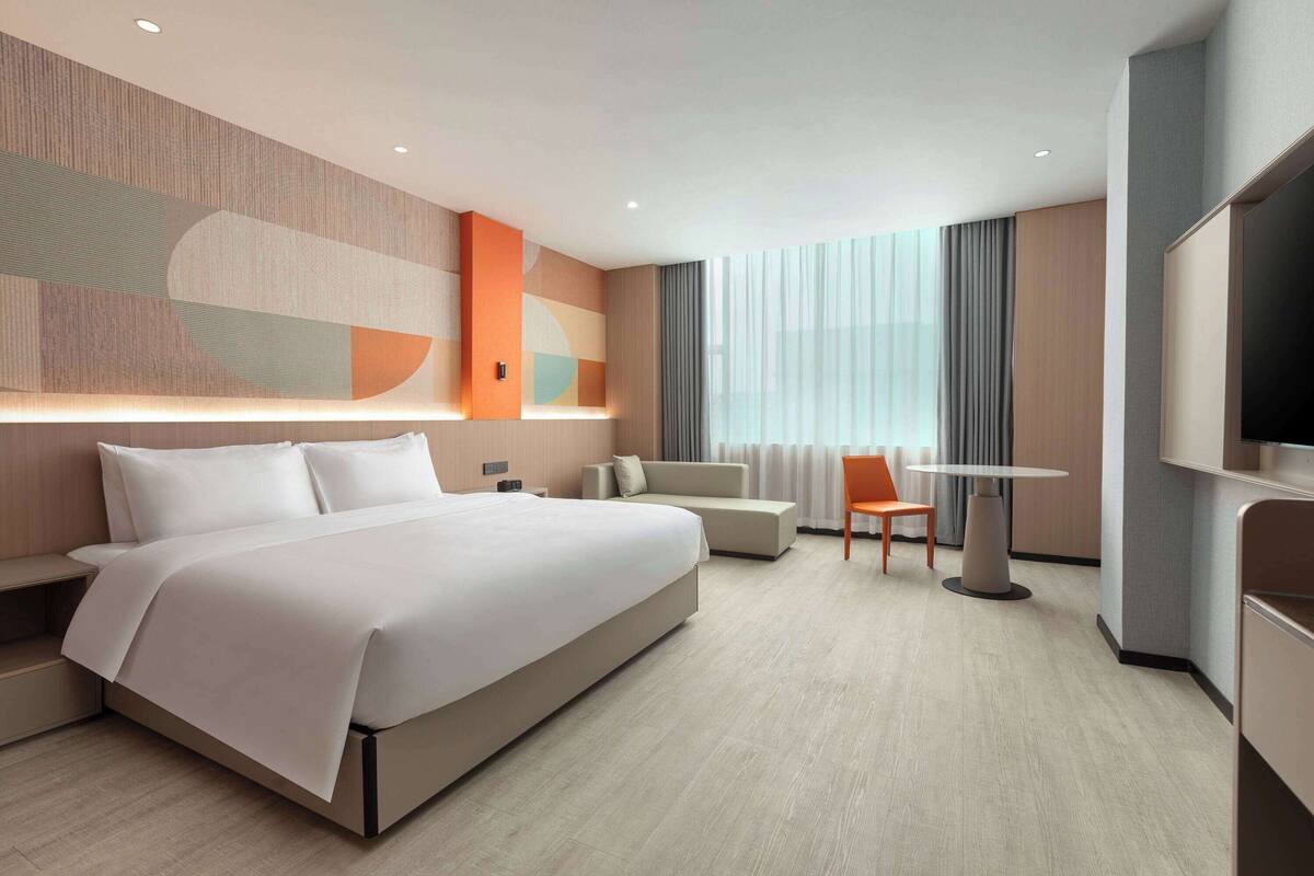 A modern hotel room with a large bed, a sofa, a dining table, and a TV.