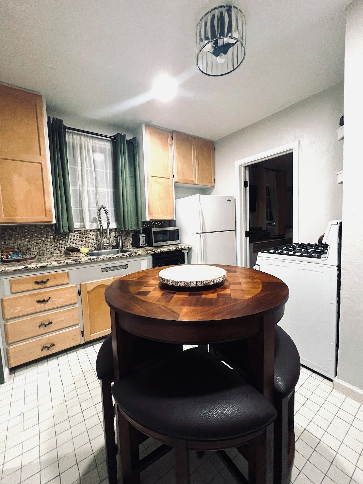 A compact kitchen with wooden cabinets, a microwave, a refrigerator, and a round wooden table with chairs.