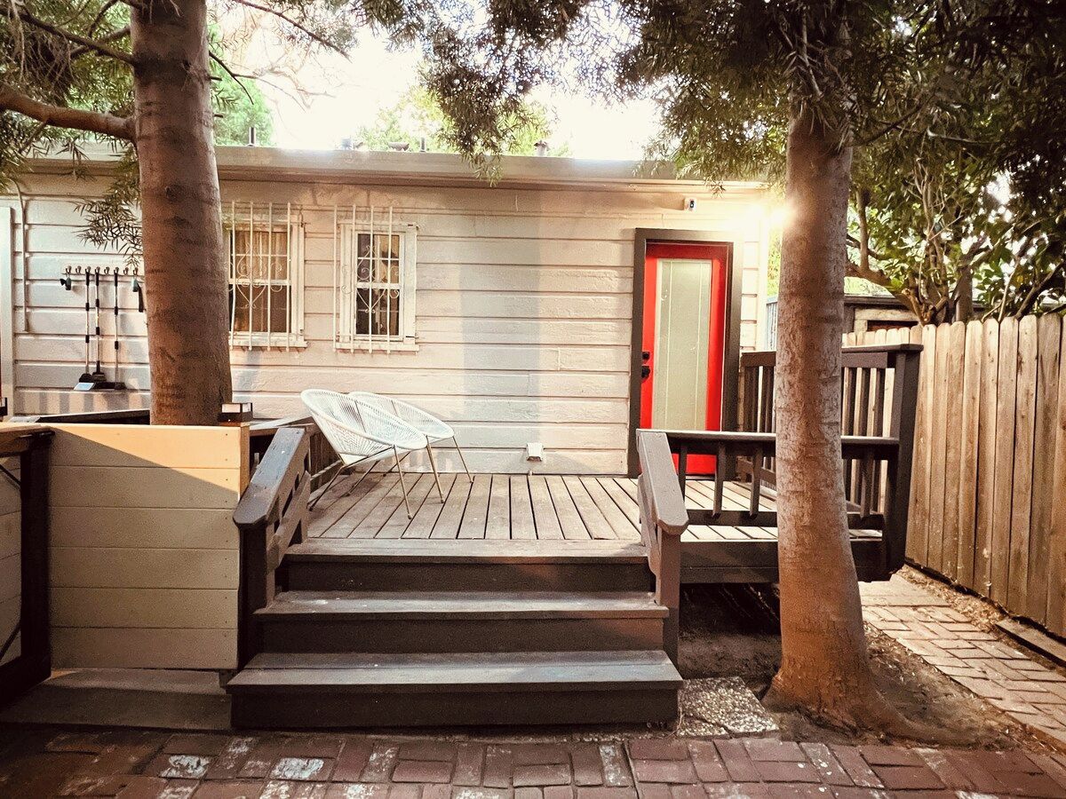 Una terraza de madera con escalones que conducen a una puerta, rodeada de árboles y una cerca.