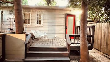 Una terraza de madera con escalones que conducen a una puerta, rodeada de árboles y una cerca.