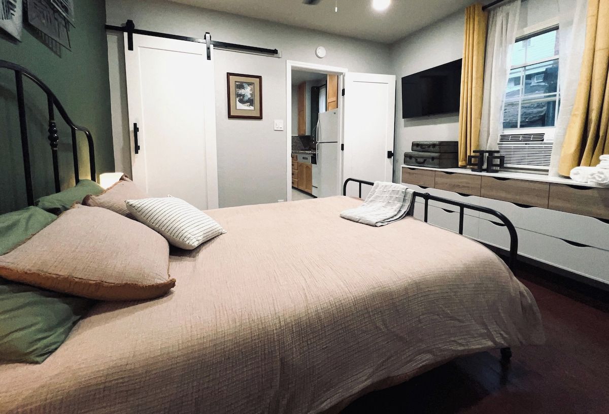 A bedroom with a bed, a bedside table, a TV, and a window with curtains.