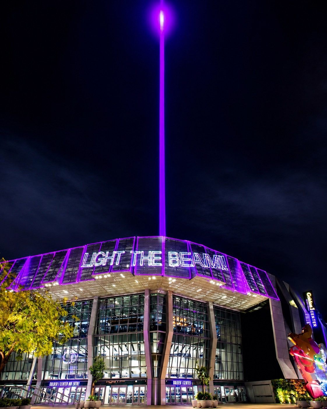 A modern building with a prominent vertical light feature and the text 'LIGHT THE BEAM' on the facade.