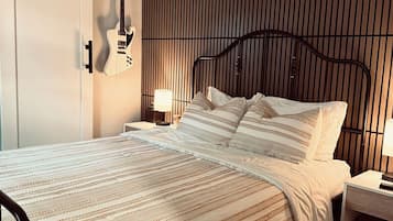 Un dormitorio con cama, mesita de noche, lámpara, guitarra y una pared con listones verticales.