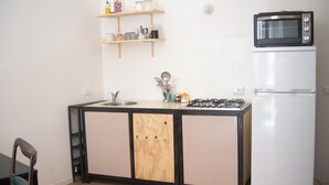 A compact kitchen with a wooden cabinet, a gas stove, a microwave, and a refrigerator. - Pannieri apartment  (Palermo)