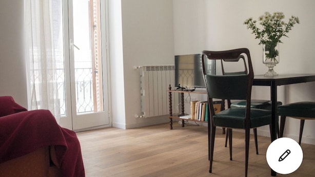 A room with a wooden floor, a green chair, a table with a vase of flowers, and a bookshelf. - Pannieri apartment  (Palermo)