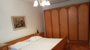 A neatly made bed in a room with a wooden wardrobe and a painting on the wall.