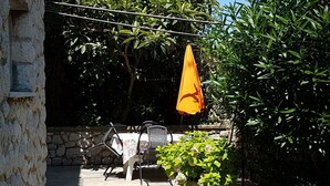 A stone wall, outdoor table with chairs, and an orange umbrella in a garden setting.