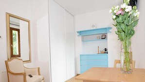 Una habitación con una mesa de comedor de madera, una silla, un espejo, un armario azul y un jarrón con flores.