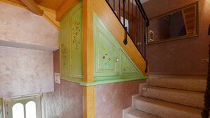 Una escalera con escalones color beige y barandal verde, que lleva a un rellano con techo de madera y una puerta con ventana de vidrio esmerilado.