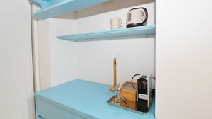Una habitación con un escritorio azul y cajones, una tetera, una taza y un pequeño taburete de madera.