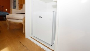 Una habitación con un refrigerador blanco etiquetado 'Blitz', una silla de madera y una cama con cubierta azul.